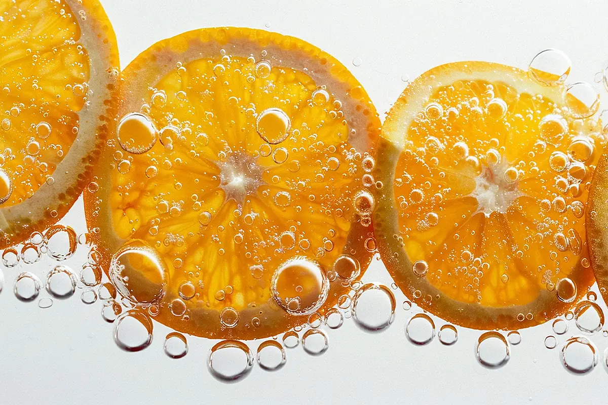 Fresh orange slices with water bubbles, visualizing vitamin C as a natural brightening ingredient in cosmetic formulations