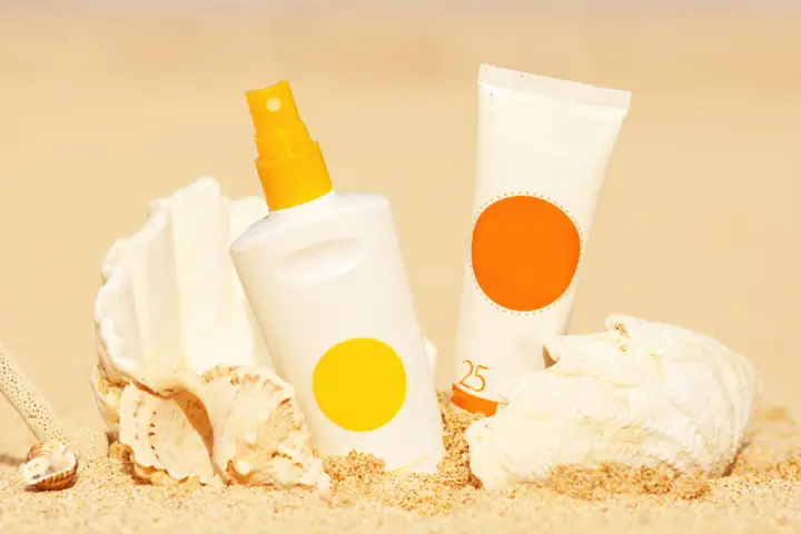 Image of sunscreen spray and sunscreen tube on beach sand, representing Australian sun care products, sunscreen manufacturing, and summer SPF product development