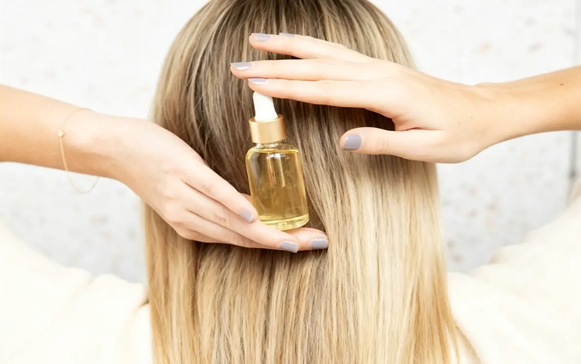 Hair oil bottle applied to blonde hair for private label hair growth and scalp care products