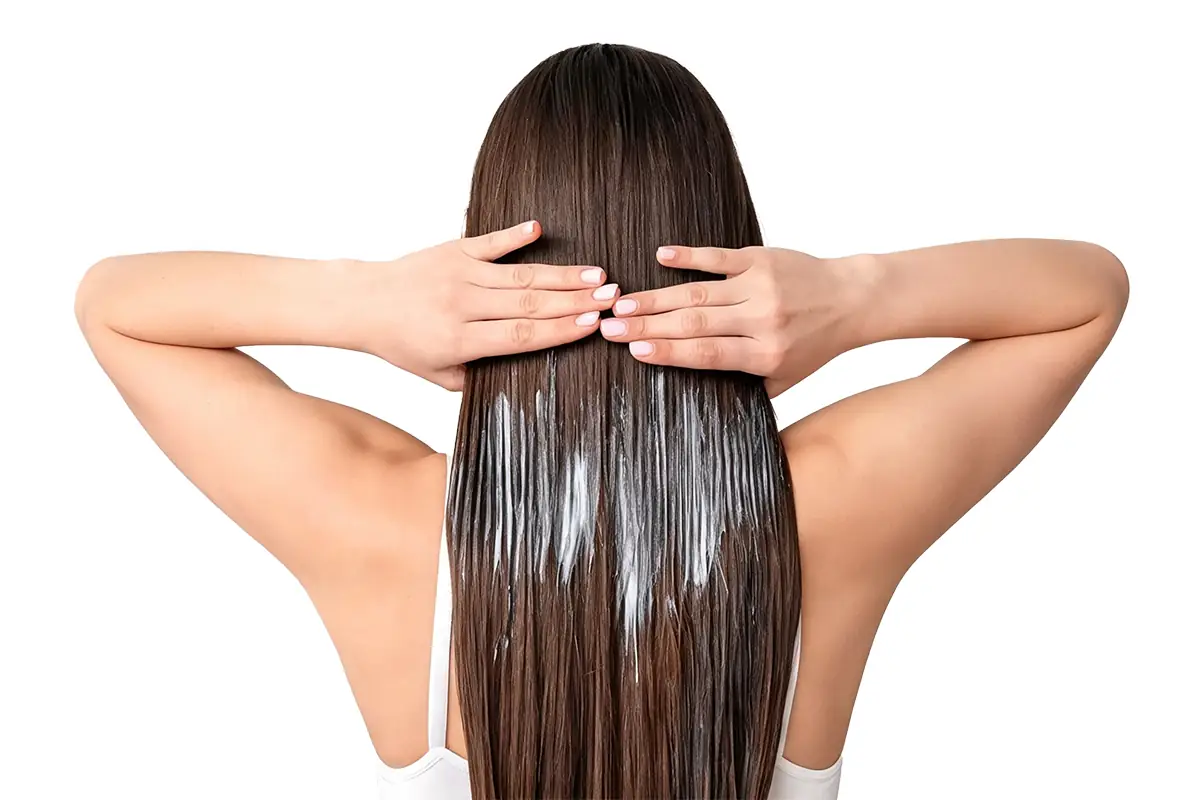 Woman applying a rich hair conditioner treatment to long hair for softness, detangling, moisture, and damage repair